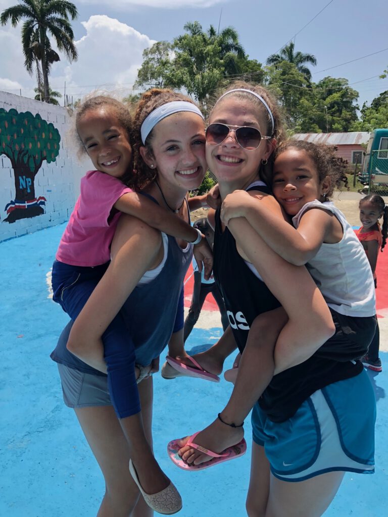 Teenage girls hold small children on their backs.