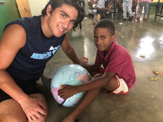 A young adult and child sit on the floor with a globe.