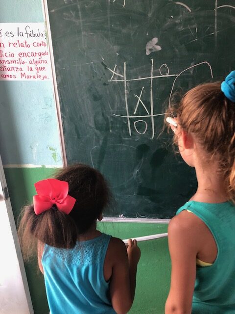 A young adult and child play tic-tac-toe on a chalk board.
