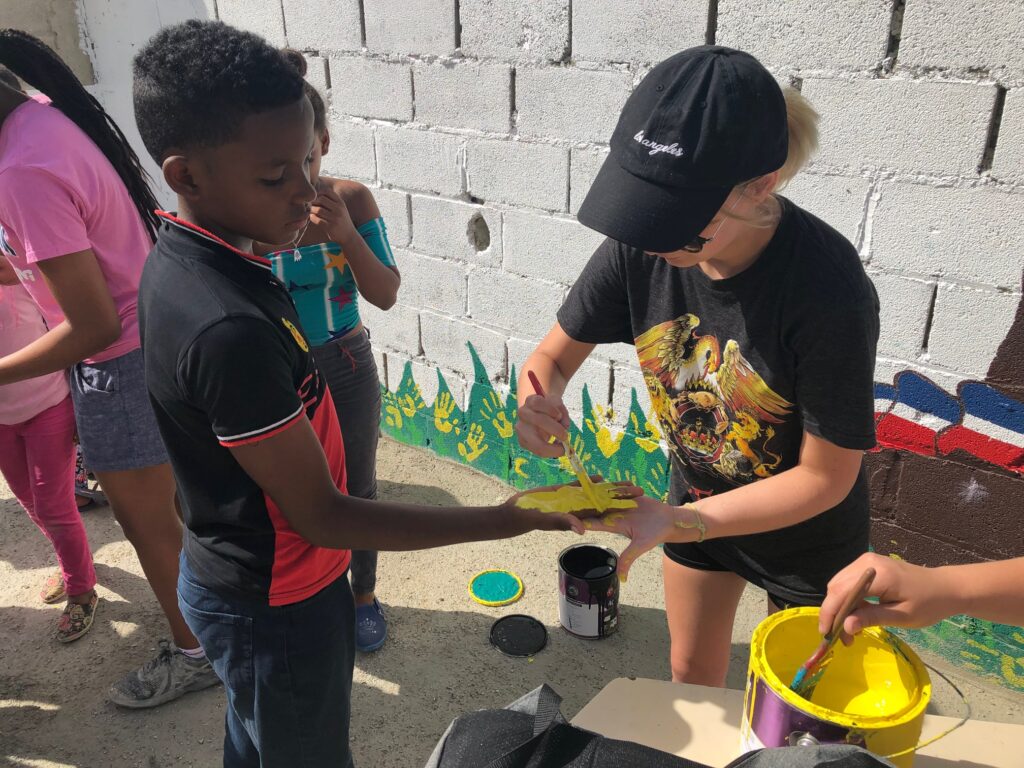 A young adult paints on a child's hand.