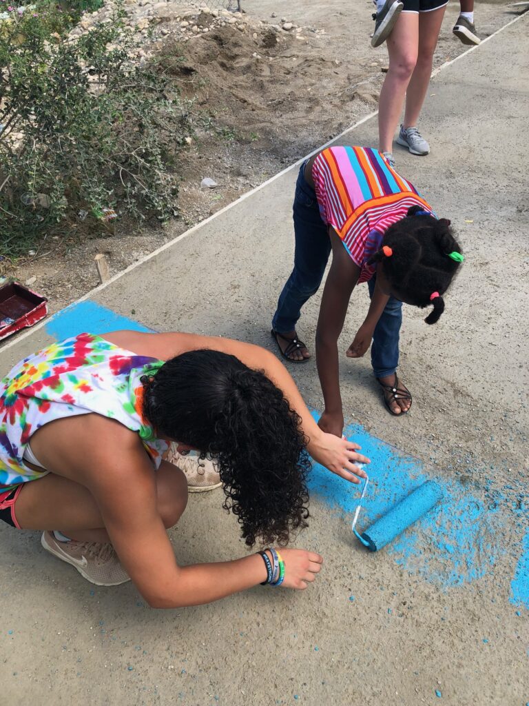 A young adult and child paint on the sidewalk.