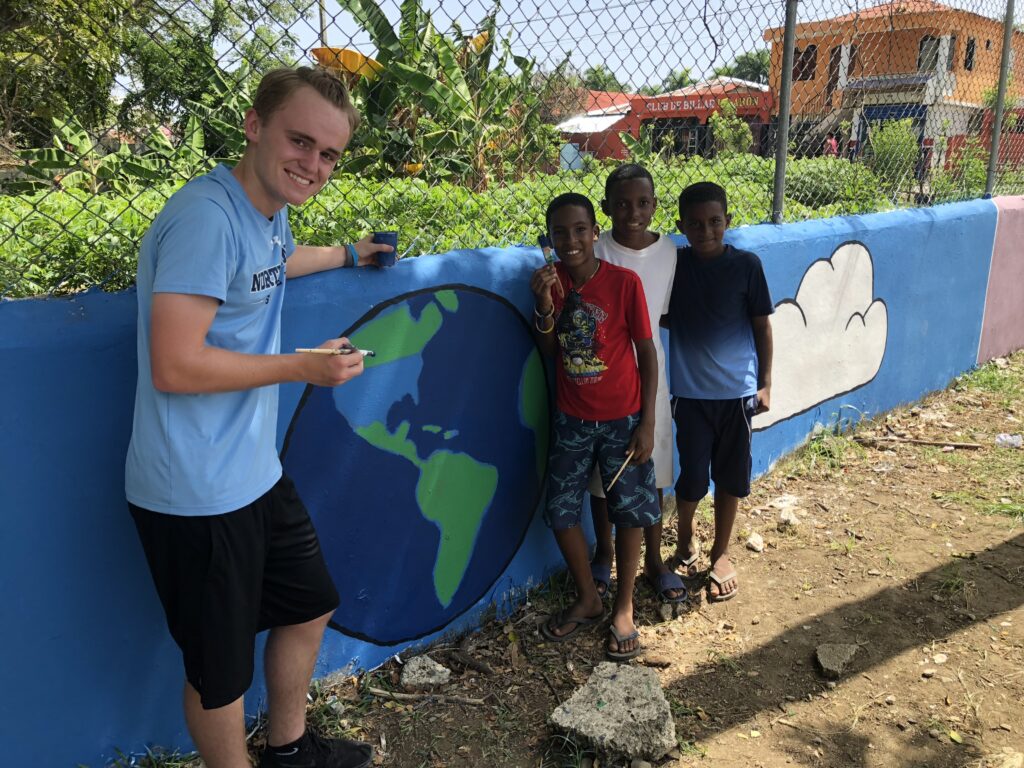 A young adult and children stand in front of a earth and clouds mural.