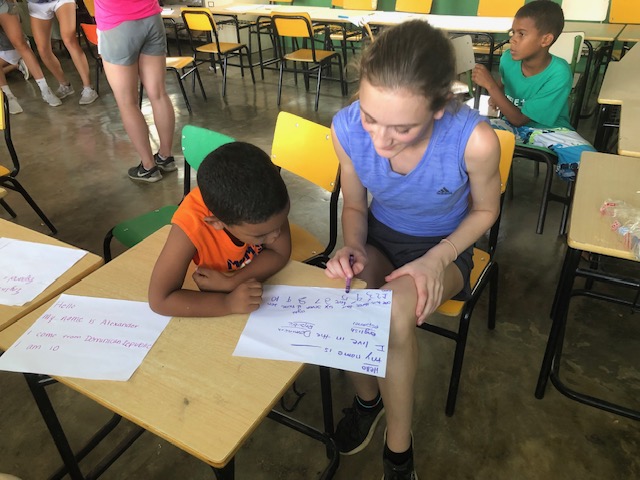 A young adults sits with a child at a desk looking at papers.