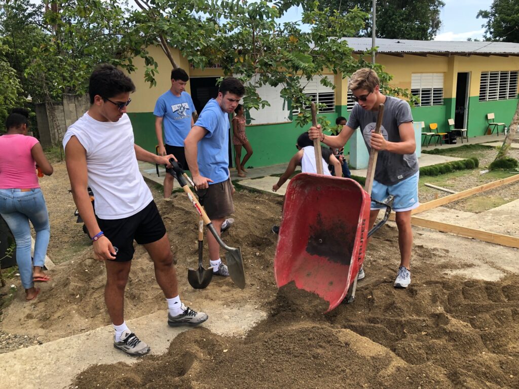 Young adults work on move dirt with a wheel barrow.